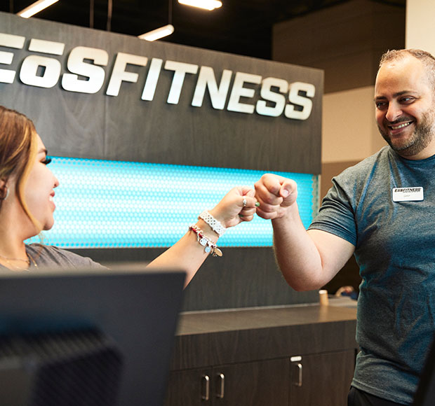 two eos staff standing behind the front desk smiling at each other and fist bumping